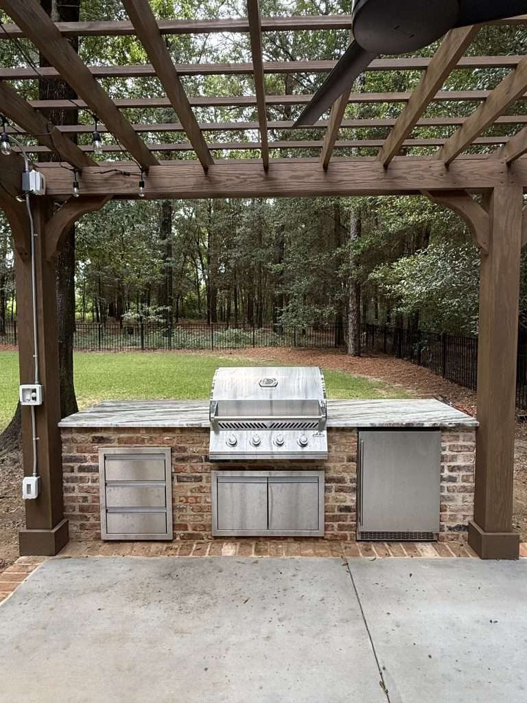 Brick outdoor kitchen with built-in grill under a wood pergola, built by Red Branch Outdoor Living